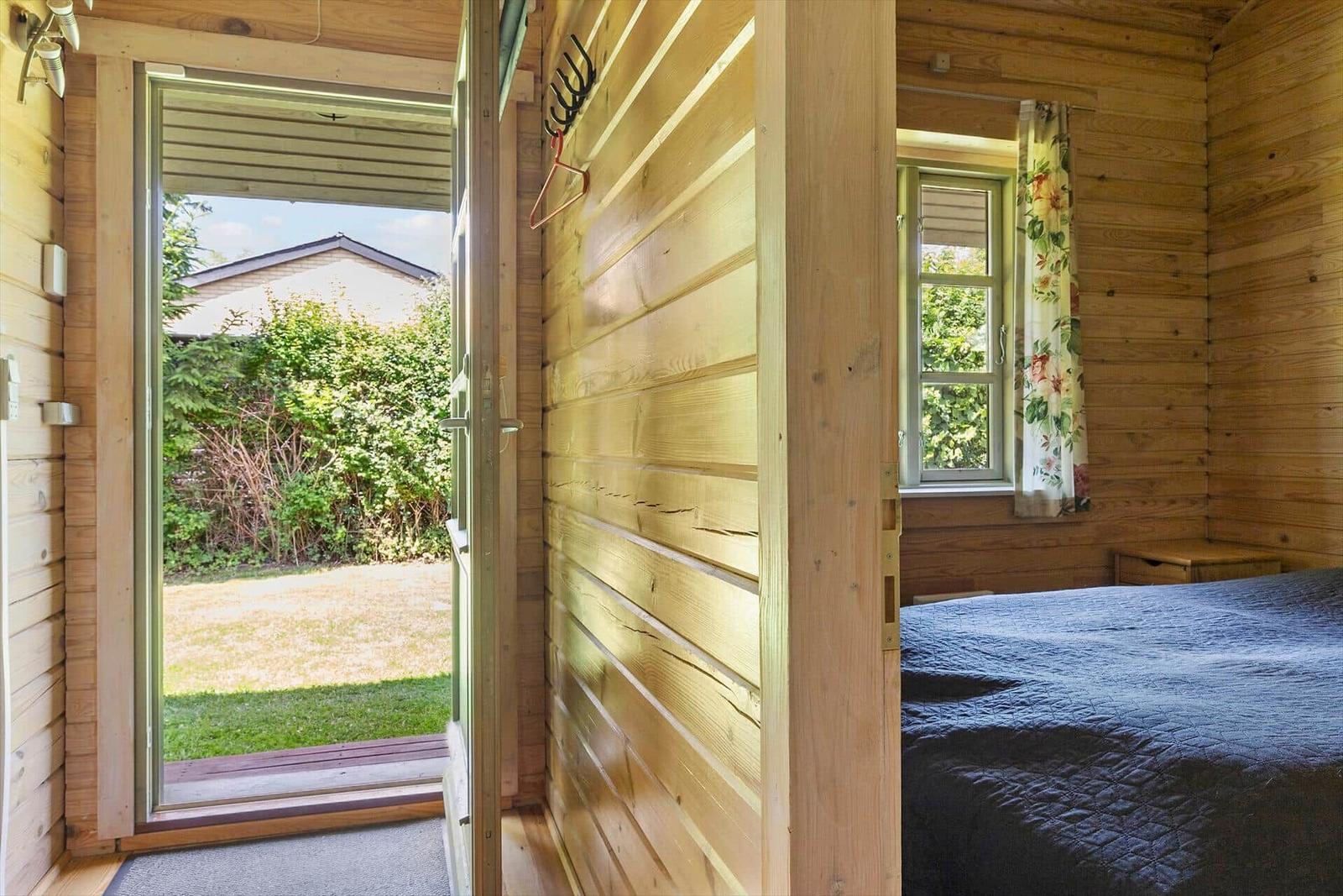 Schlafzimmer mit Holzwand, Bett und Fenster mit Blumenvorhang.