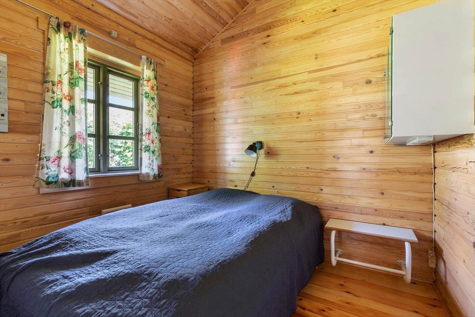 Schlafzimmer mit Holzwand, Bett, Fenster mit Vorhängen und Wandlampe.