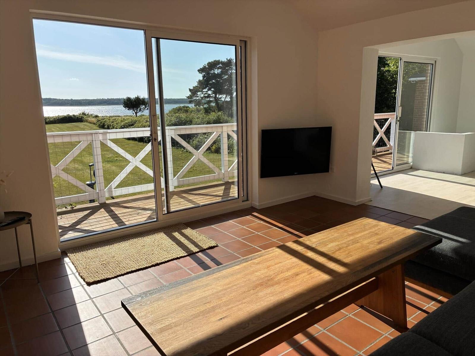 Wohnzimmer mit Blick auf Wasser, Holztisch und Fernseher an der Wand.
