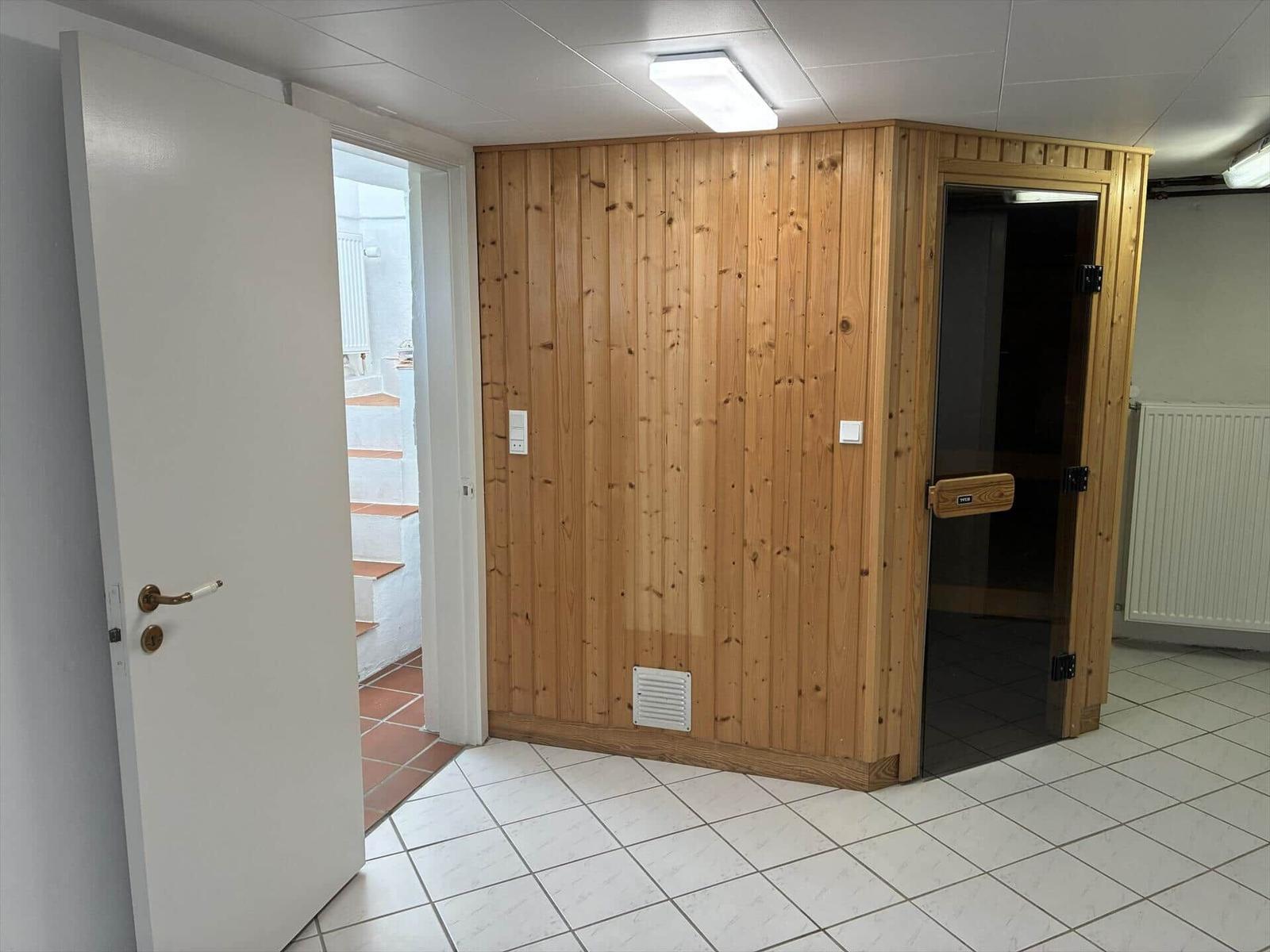 Sauna mit Holzwand und Tür im Raum mit Fliesenboden.