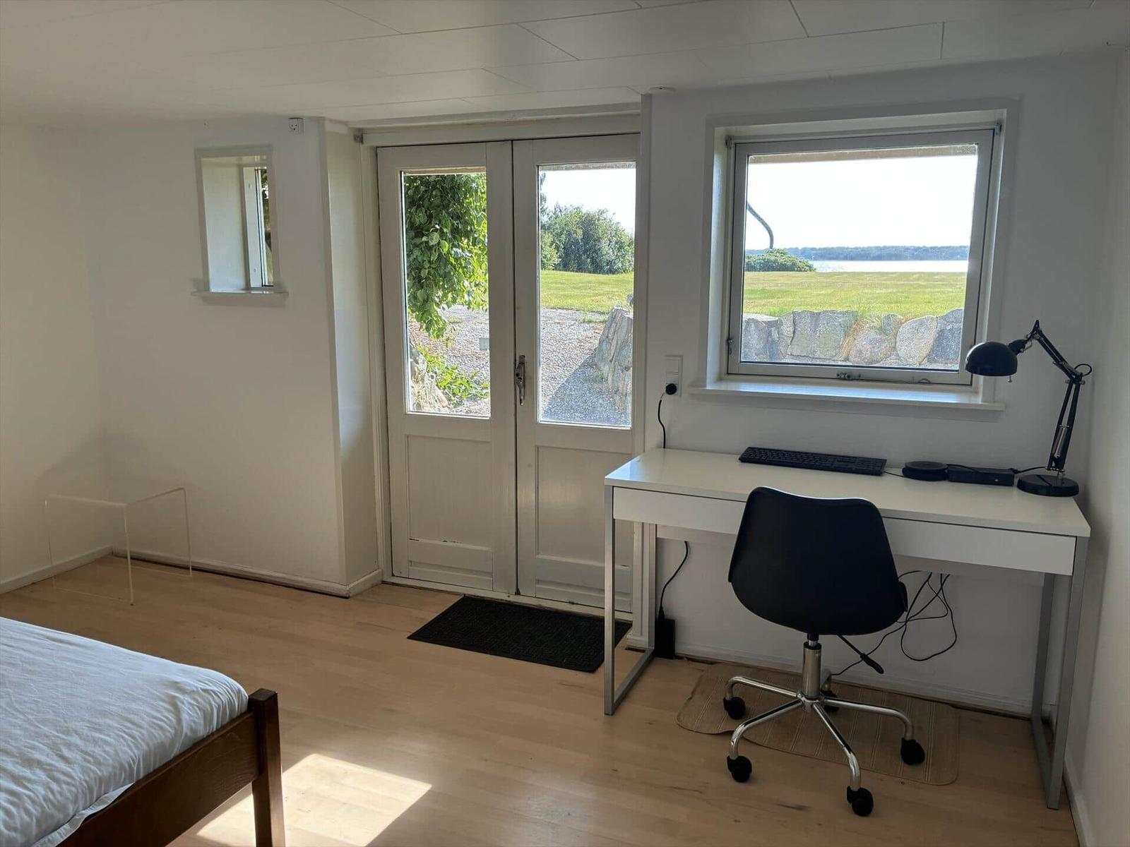 Zimmer mit Schreibtisch, Bett und Blick auf Grünland und Wasser.