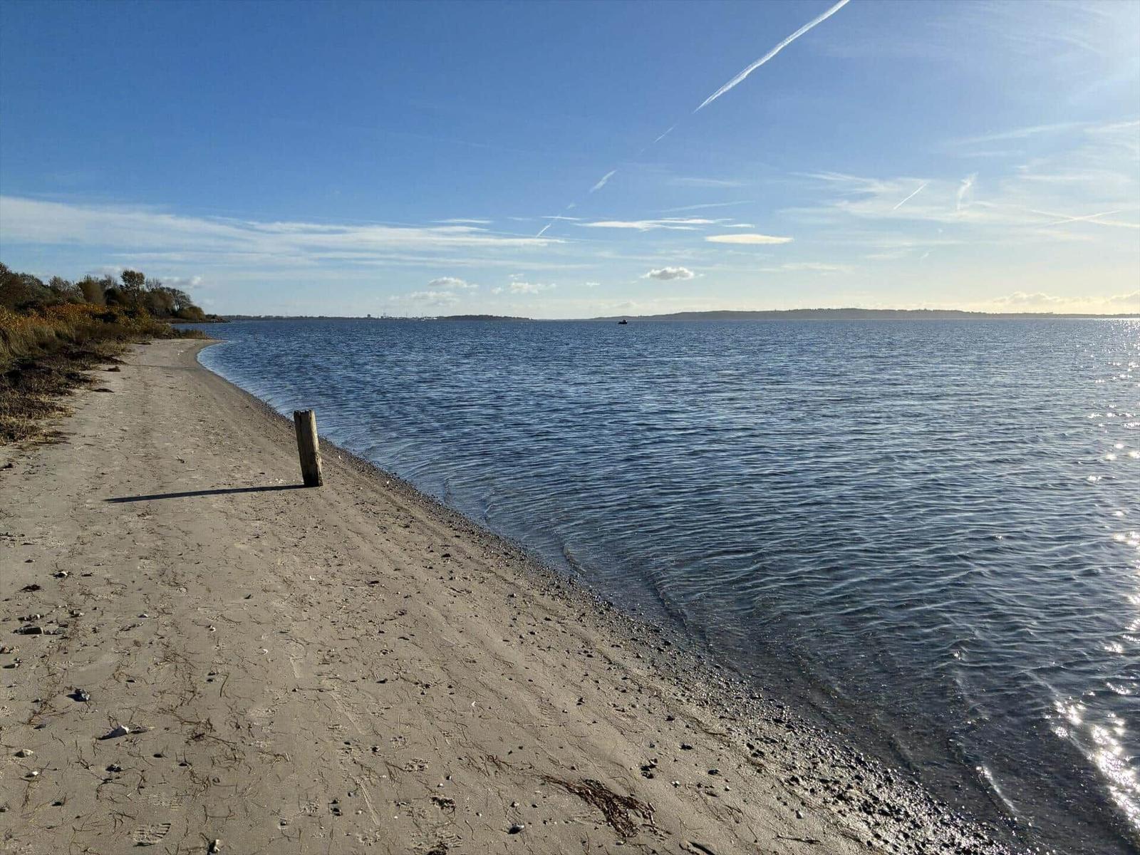 Strand mit Sand und Wasser unter blauem Himmel mit wenigen Wolken.