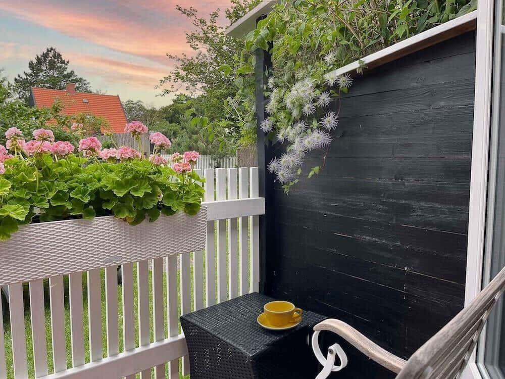 Terrasse mit Blumenkasten, Tisch und Stuhl. Blick auf Garten und Himmel.