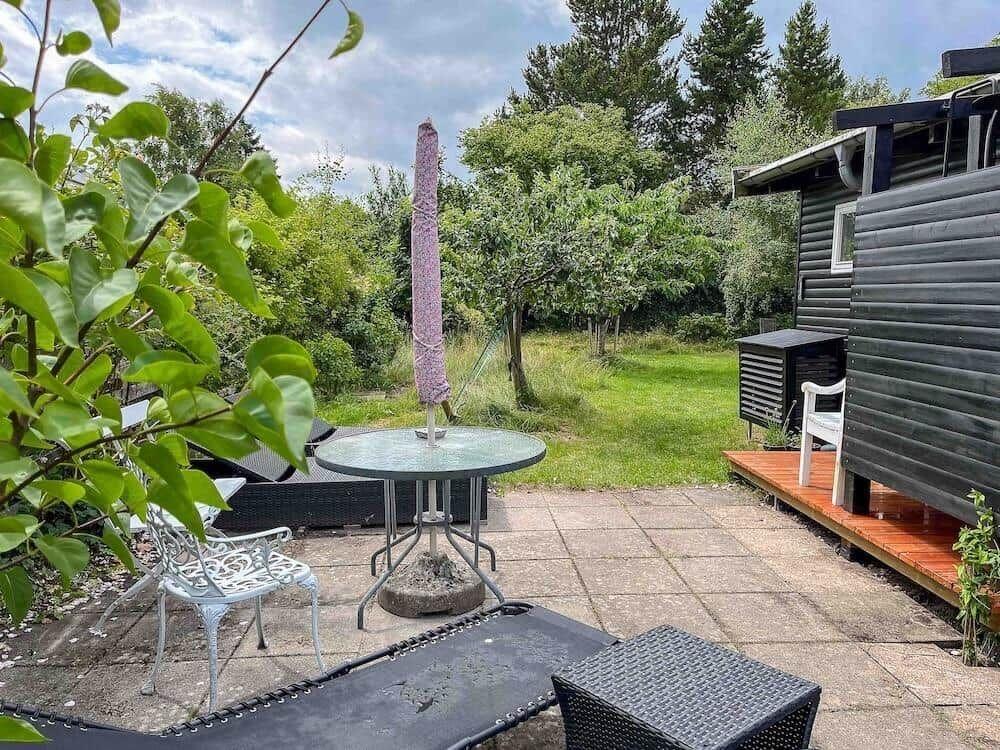 Terrasse mit Tisch, Stühlen und Schirm neben einem Holzhaus im Garten.