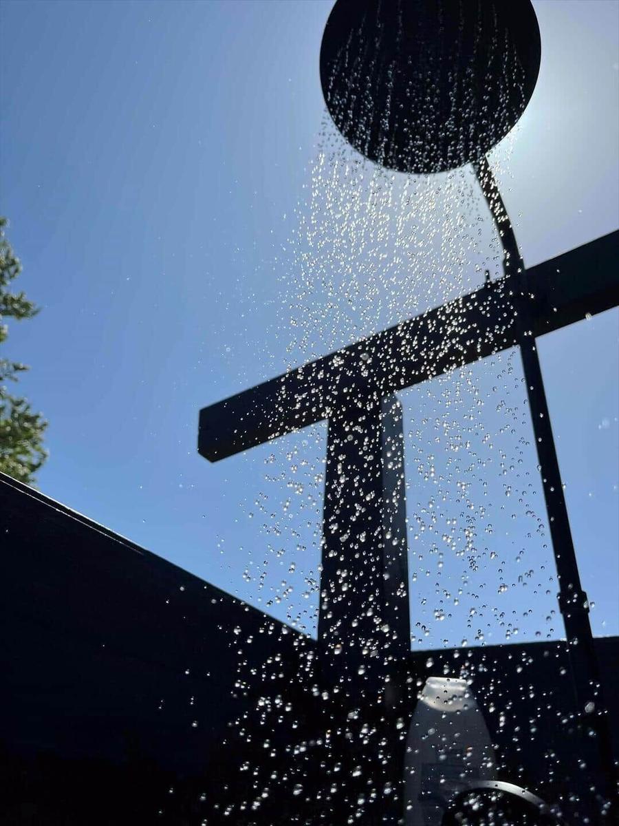 Duschkopf mit Wasserstrahl vor blauem Himmel und Holzstruktur
