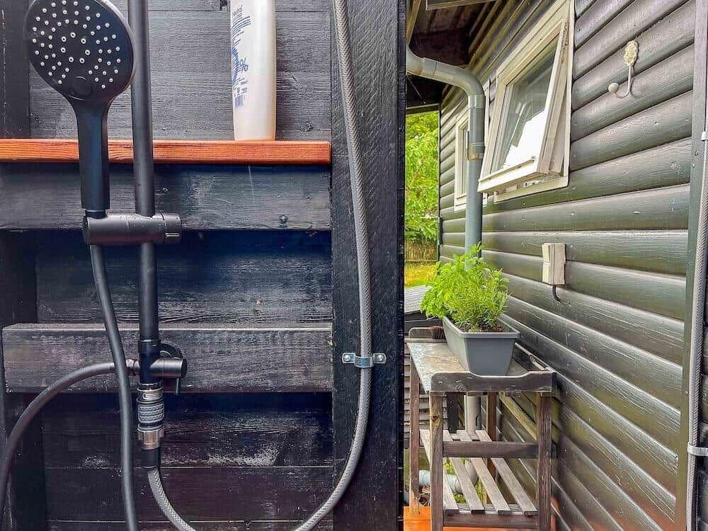 Außen-Dusche mit Handdusche und Pflanze auf Holzgestell.