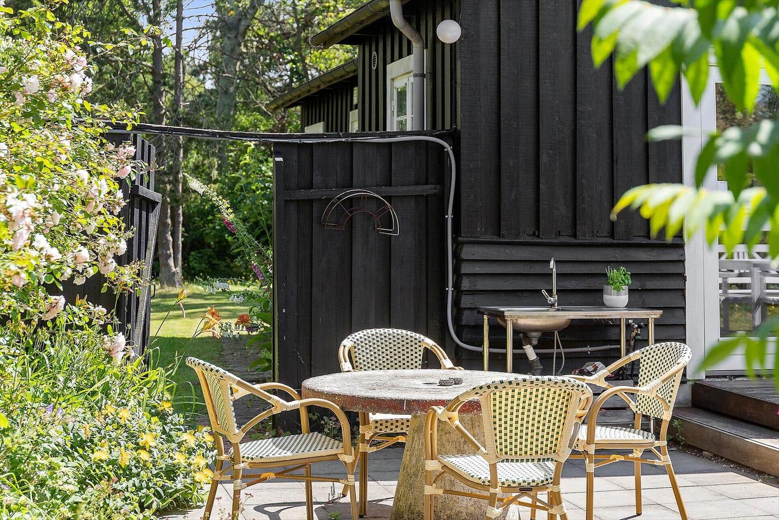 Außenbereich mit Tisch und Stühlen vor einem schwarz gestrichenen Holzhaus mit Gartentüren.