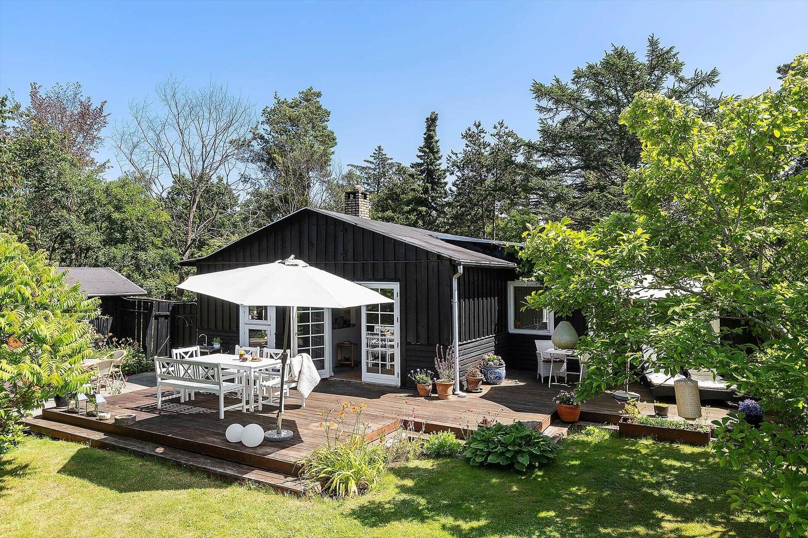 Schwarzes Haus mit Terrasse, weißer Sonnenschutz und Garten.