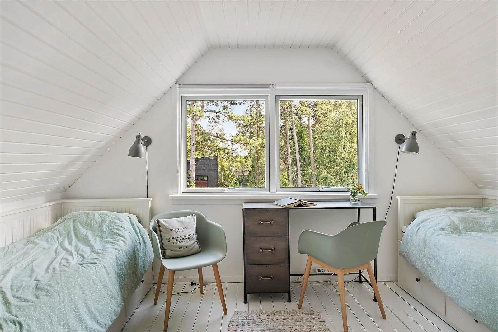Zimmer mit zwei Betten, Schreibtisch und Fenster mit Blick auf Wald.