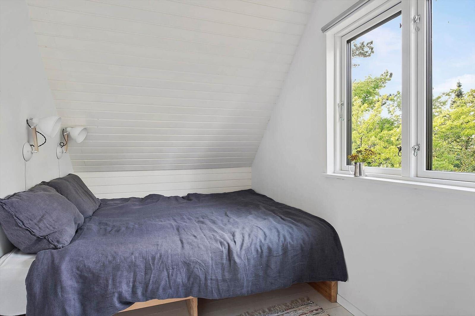 Schlafzimmer mit Dachschräge, Bett und Fensterblick auf Bäume.
