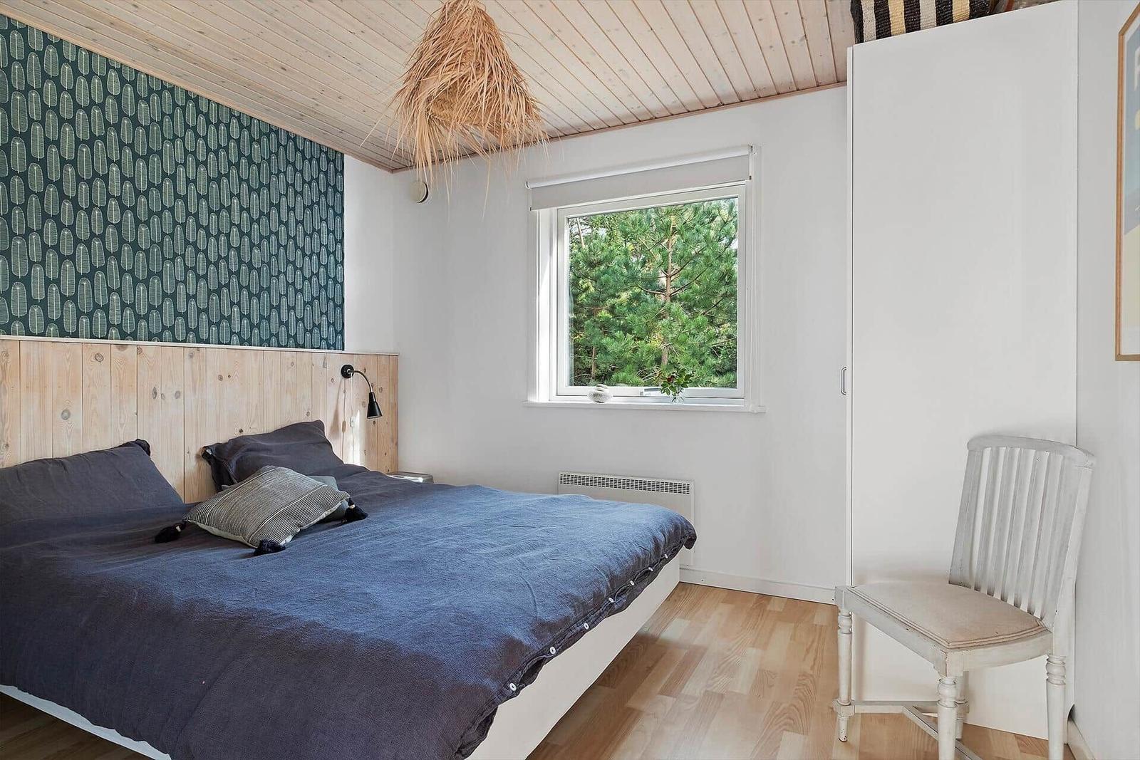 Schlafzimmer mit Bett, Fenster und Stuhl. Holzdecke und Wandverkleidung.