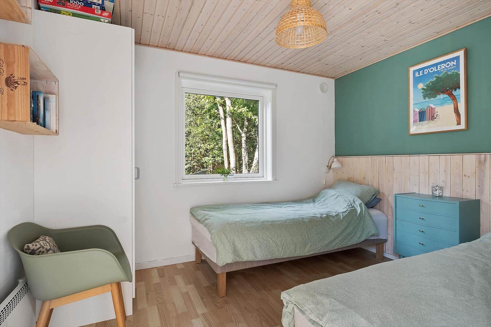 Schlafzimmer mit zwei Betten, Fenster mit Waldblick und blauem Schrank.
