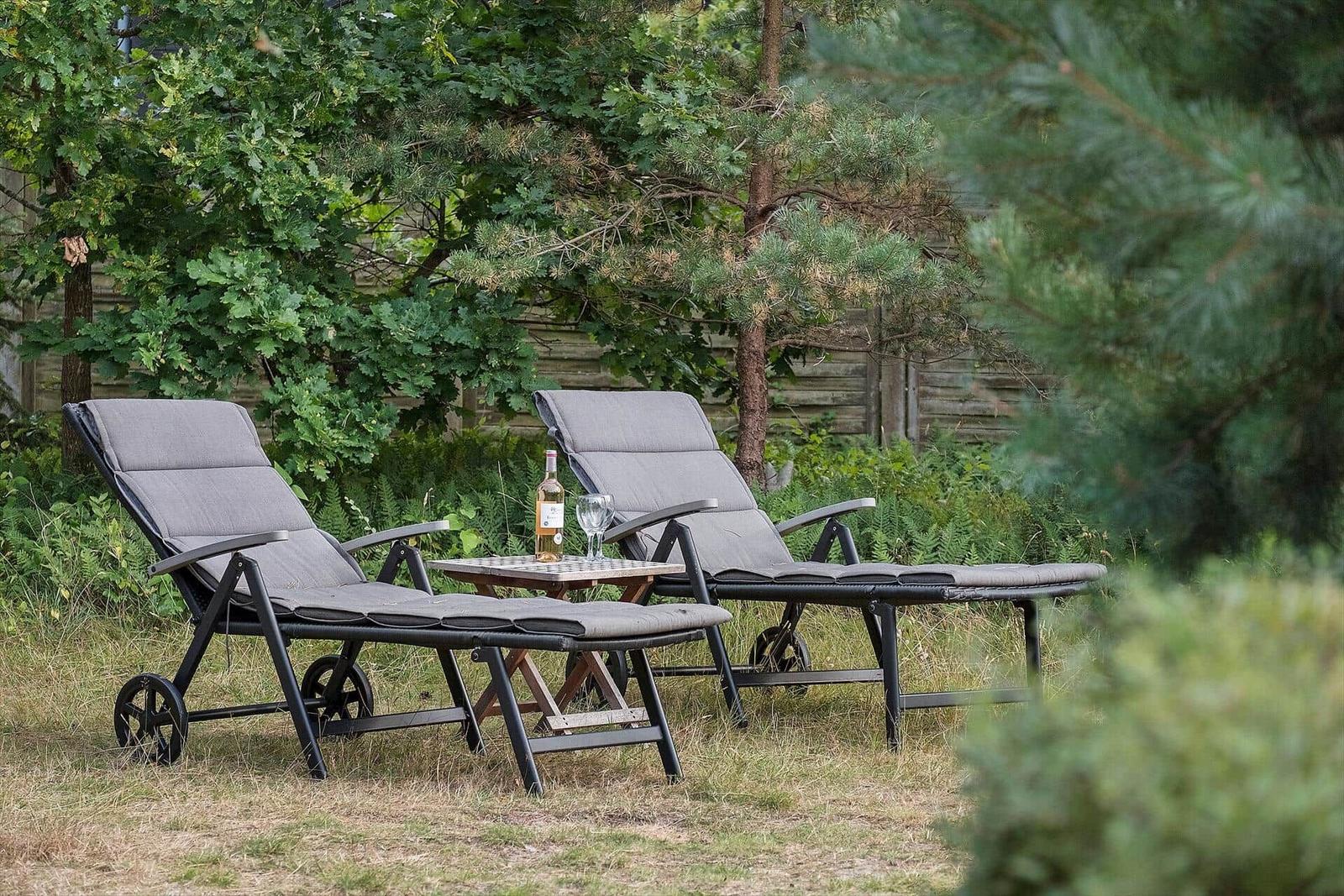 Zwei Liegestühle mit Tisch im Garten. Eine Flasche und ein Glas stehen darauf.