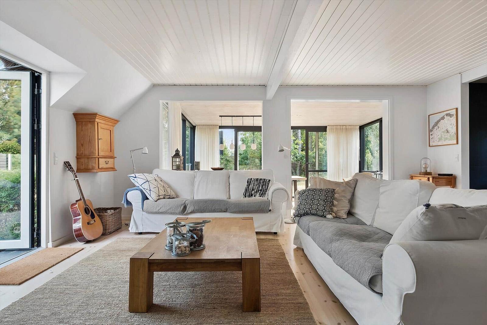 Wohnzimmer mit zwei Sofas, Holztisch und Gitarre. Durchgänge zu weiteren Räumen.