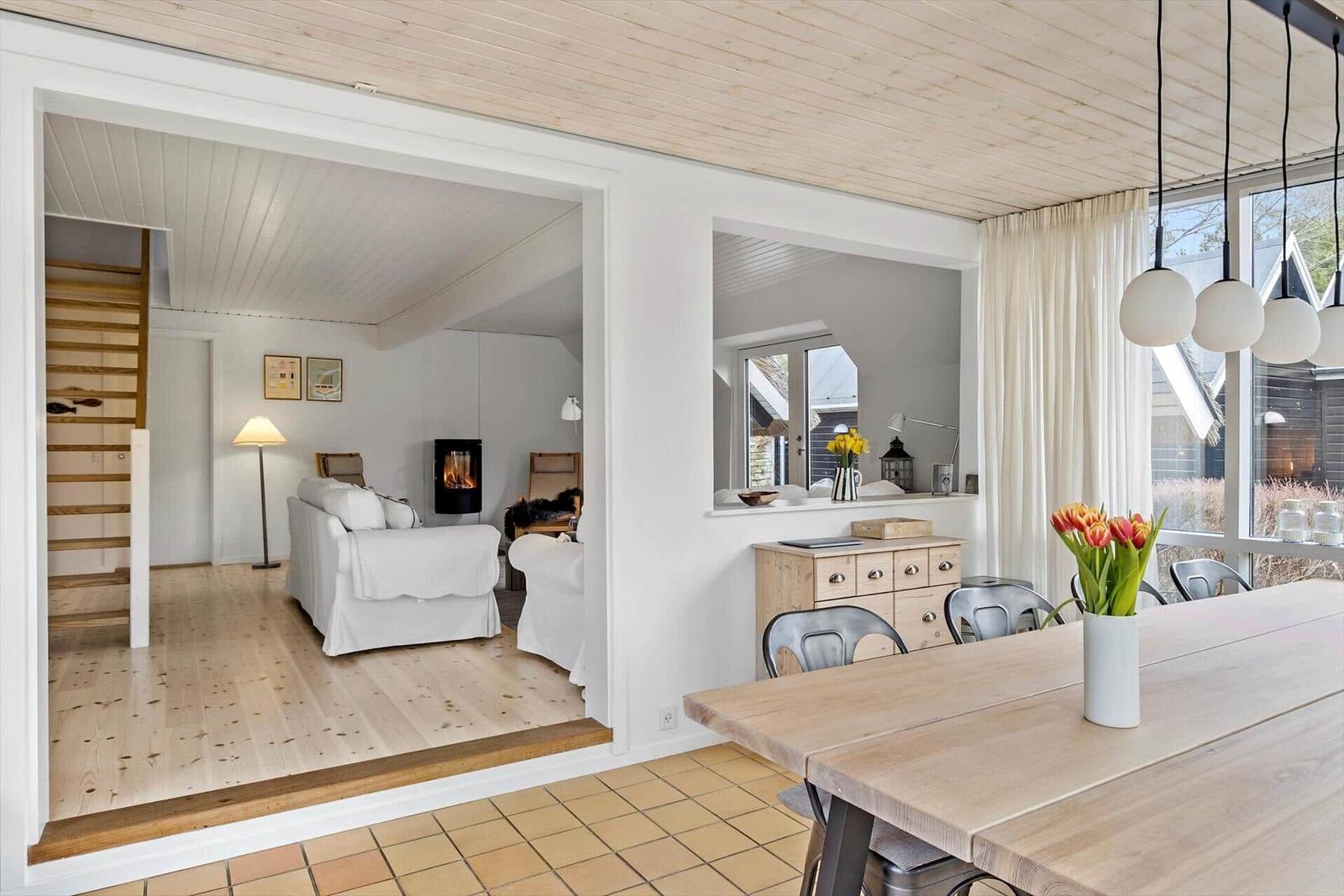 Essbereich mit Holztisch und Stühlen. Wohnzimmer mit Sofa und Kamin. Holzdecke und Boden.