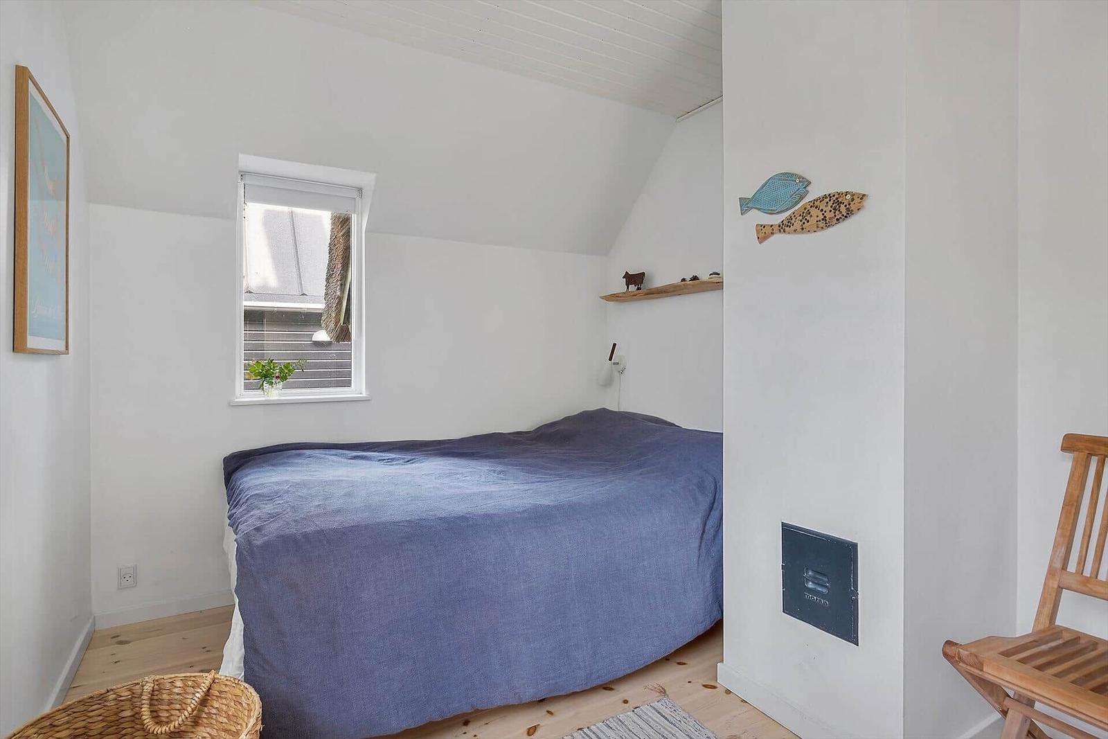 Schlafzimmer mit Bett, Fenster und Holzstuhl.