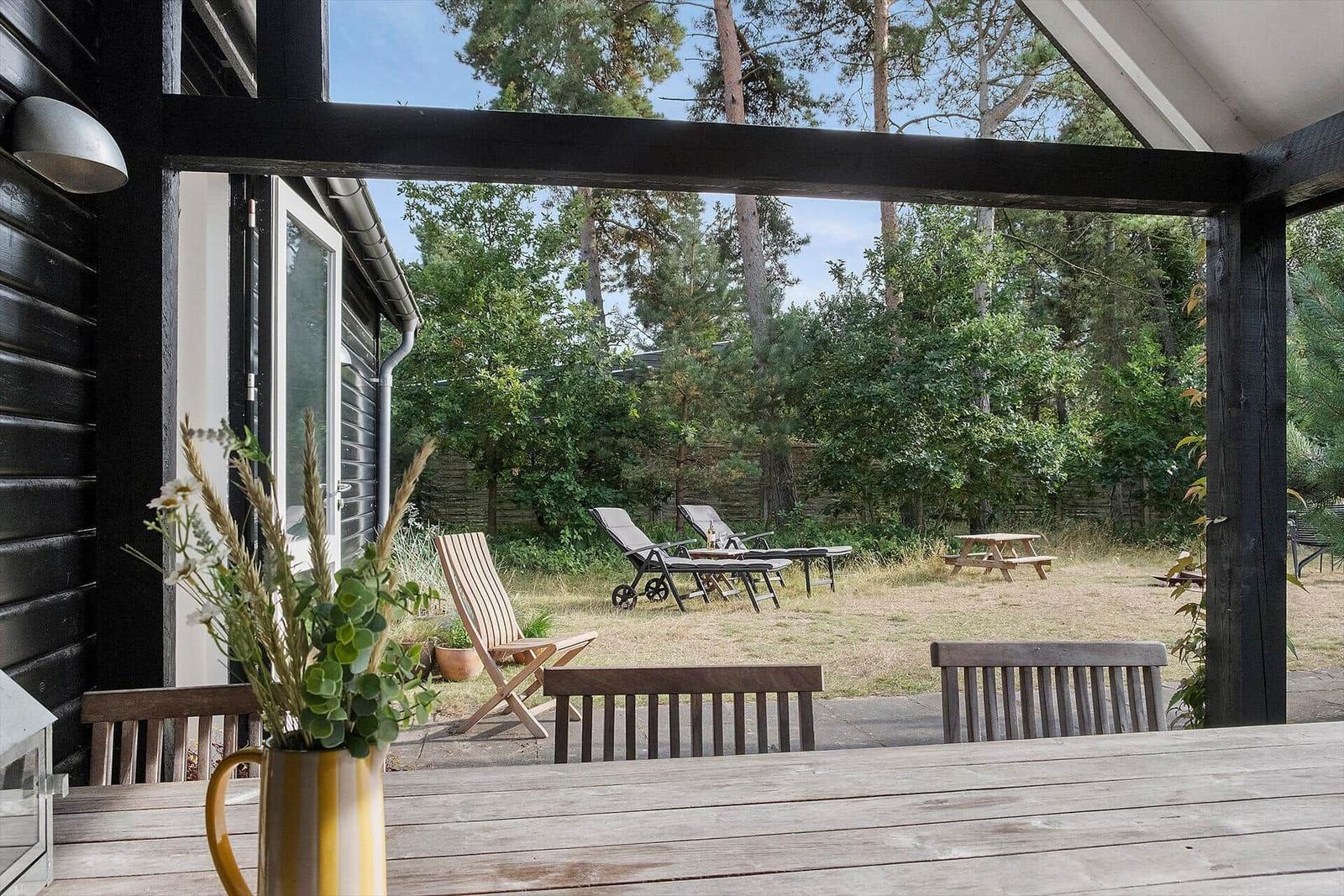 Terrasse mit Tisch und Stühlen, Blick auf Garten mit Liegen und Picknicktisch.
