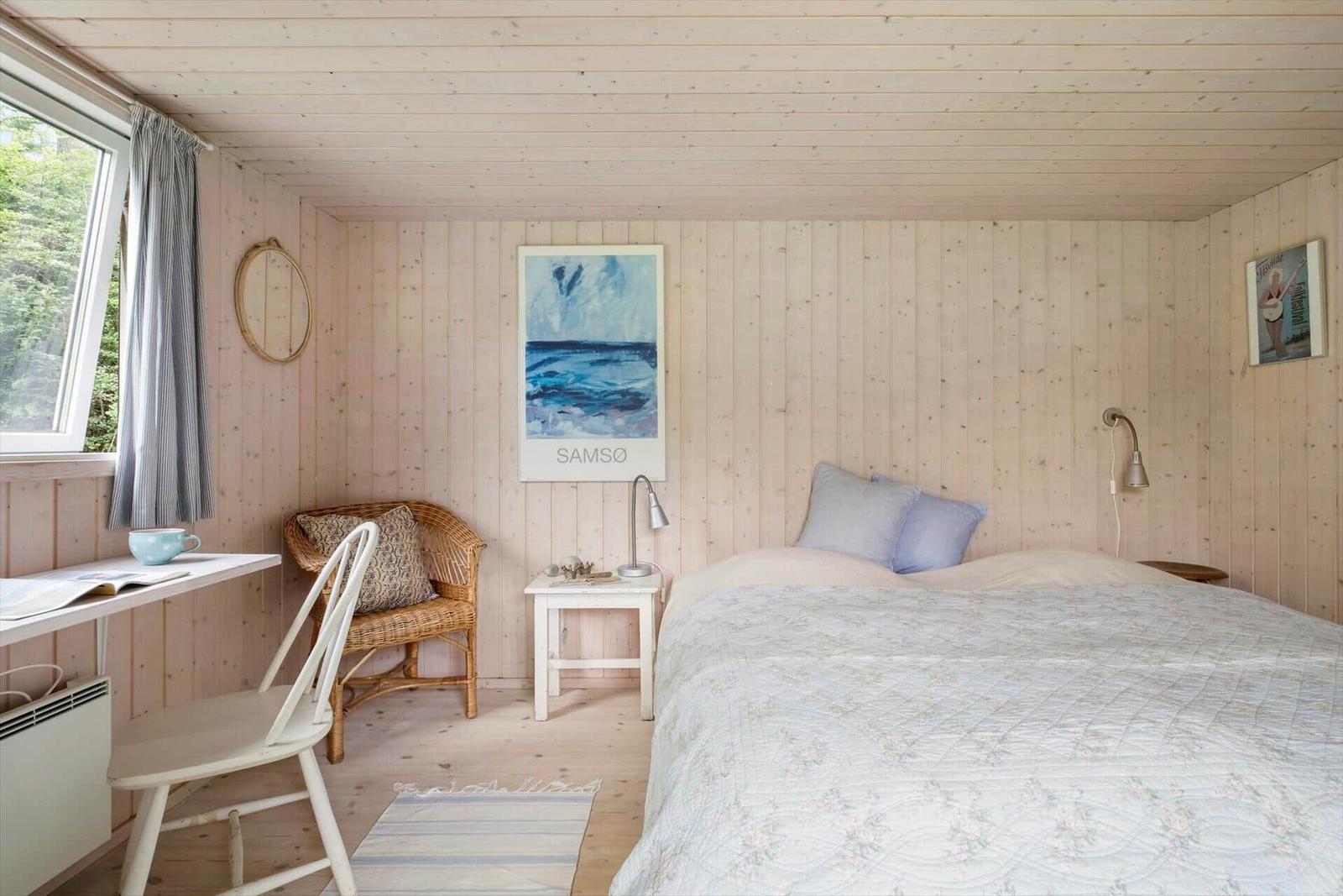 Schlafzimmer mit Bett, Nachttisch, Stuhl und Fenster.