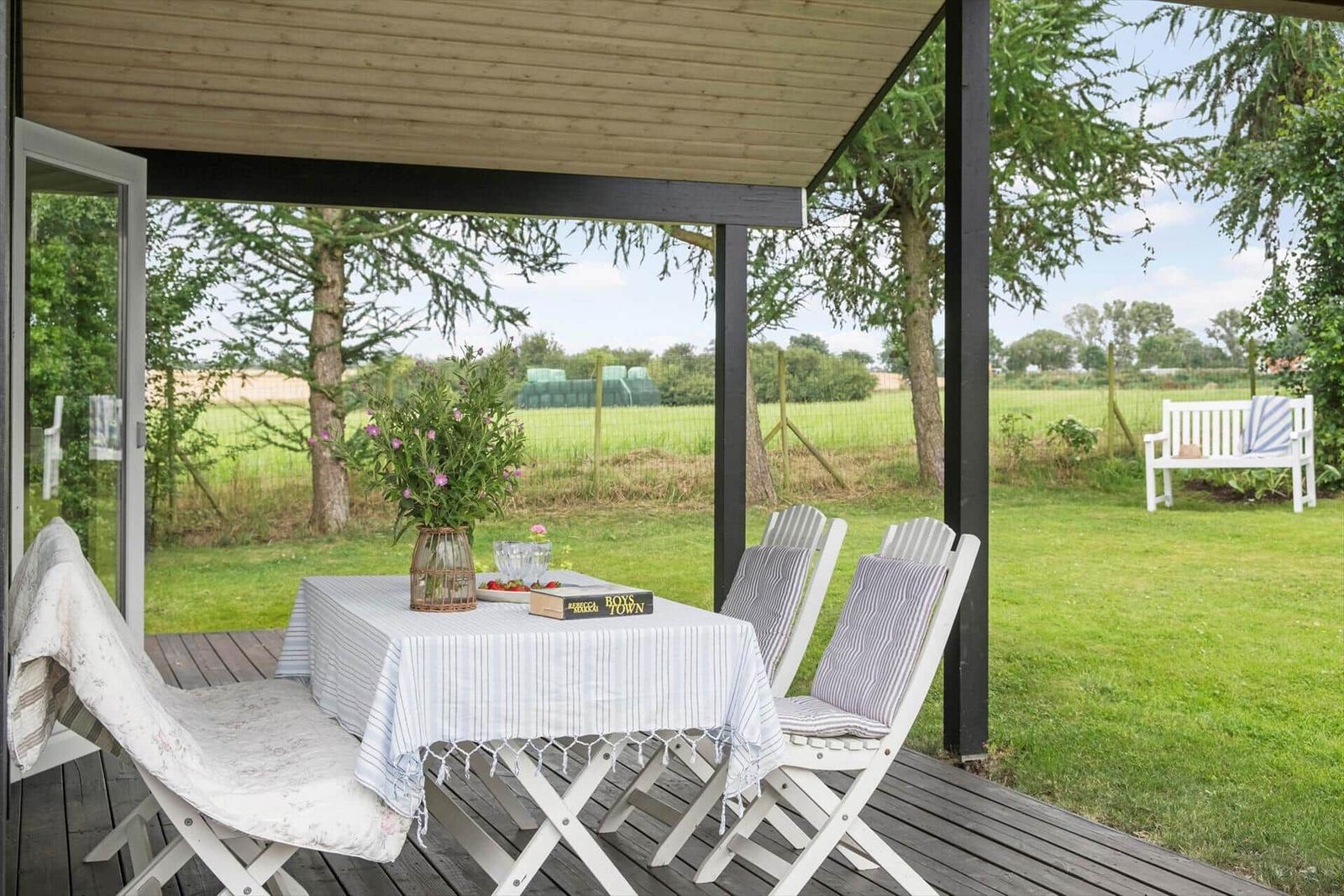 Terrasse mit Tisch, Stühlen und Blick auf grünes Feld