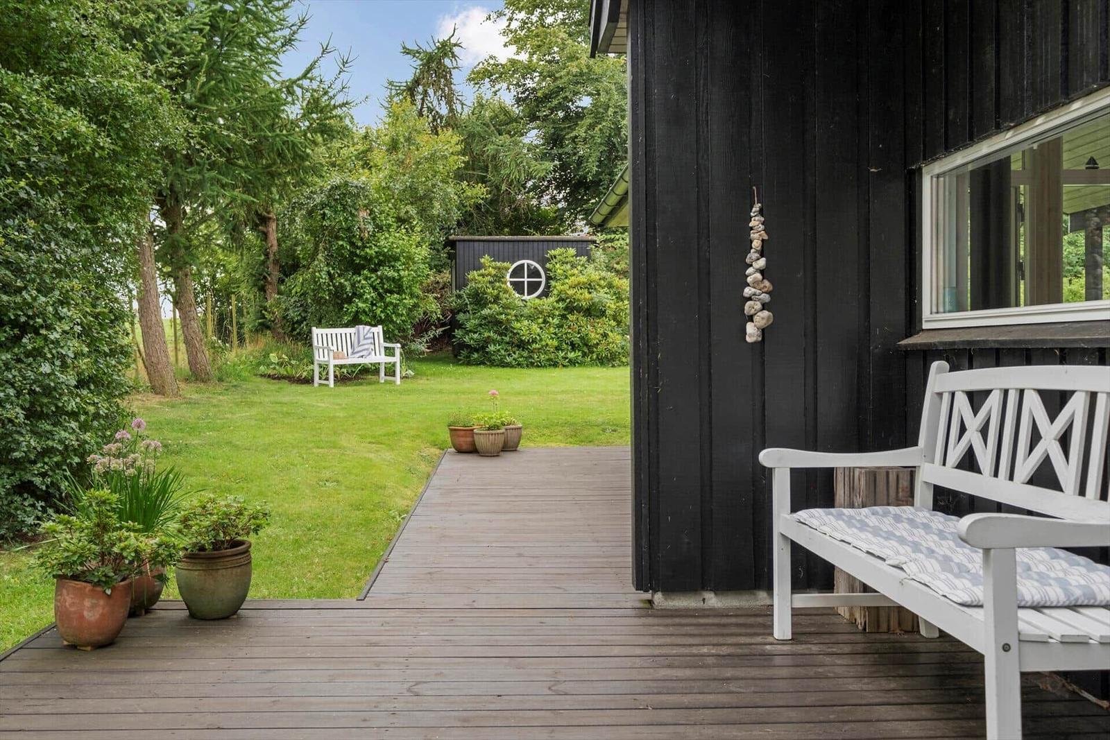 Haus mit Terrasse, Garten und weißer Bank. Pflanzen und Steinzaun sind sichtbar.
