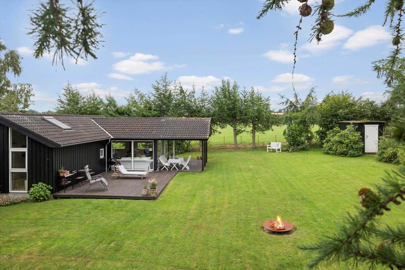 Haus mit Terrasse, Grill, Liegestühlen und Feuerkorb auf grünem Rasen.