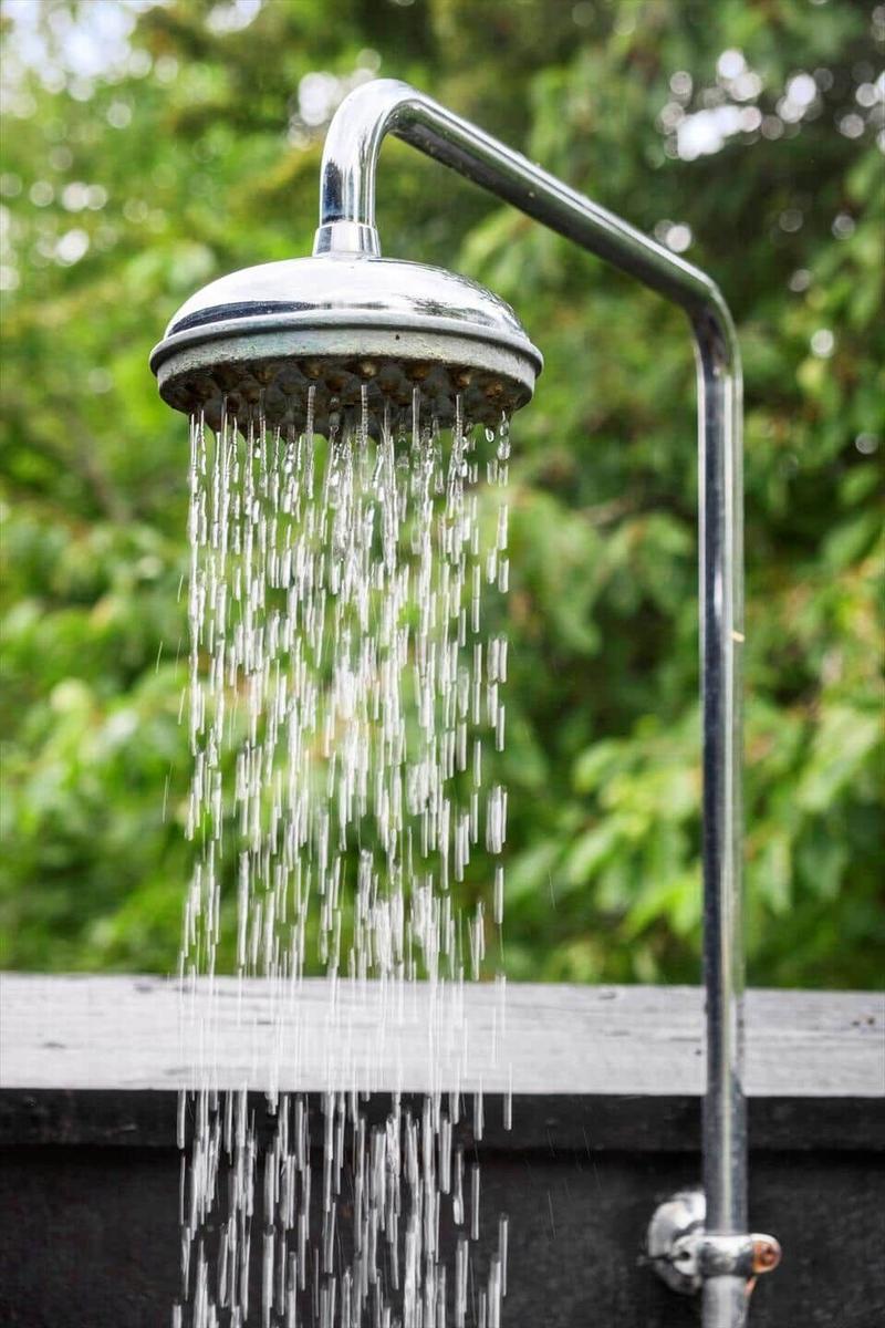 Außendusche mit Wasserstrahl und grüner Hintergrund