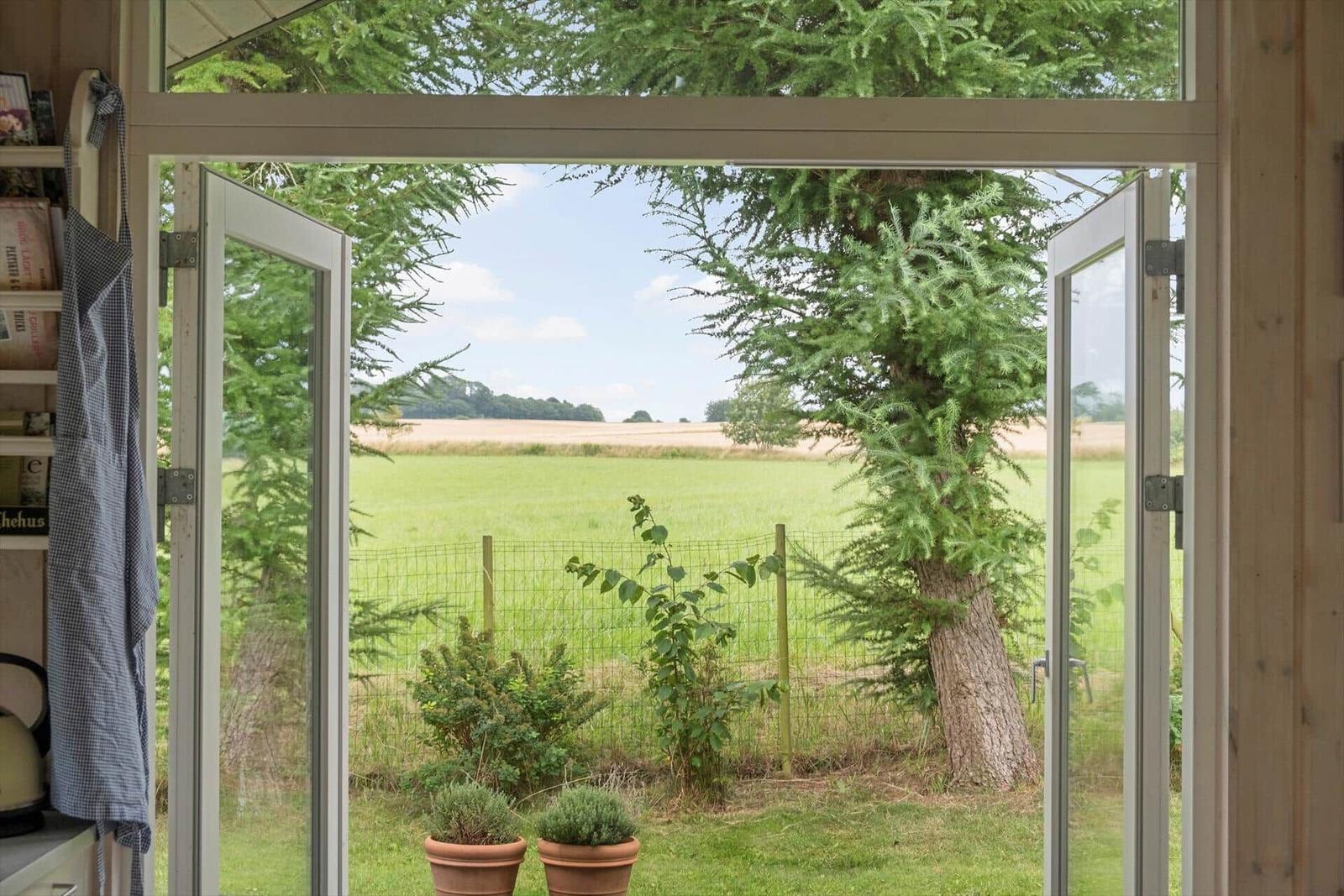 Durch offene Fensterblick auf grünes Feld und Baum.