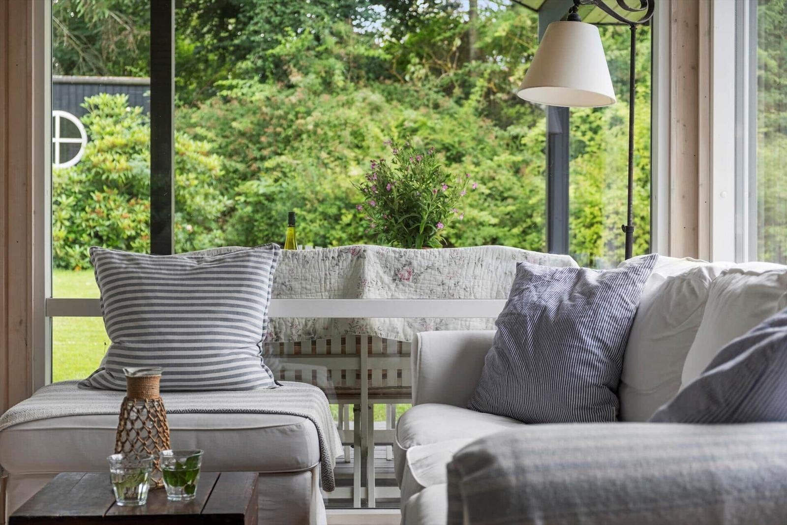 Sitzbereich mit Sofa und Kissen vor großem Fenster mit Blick auf Garten.