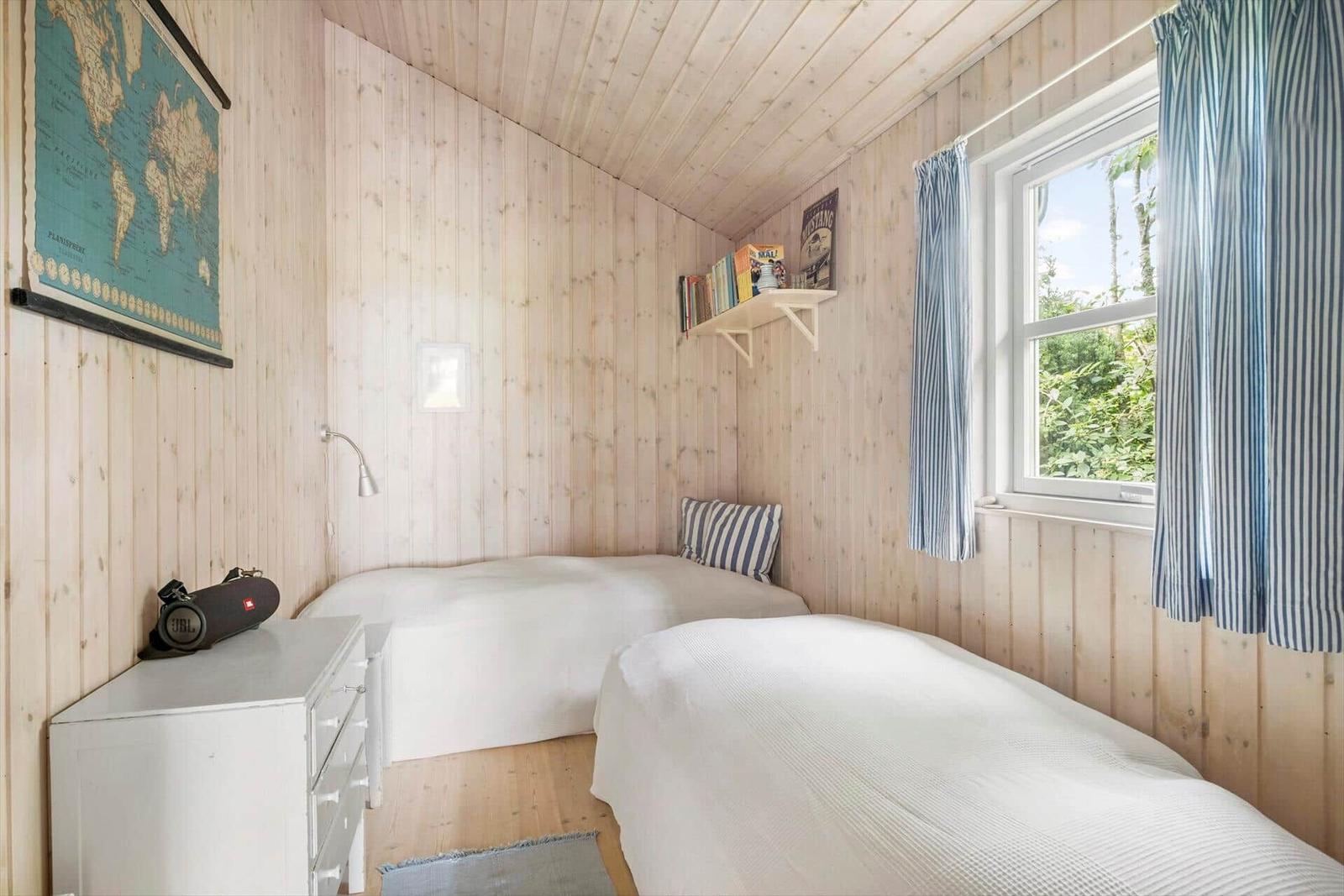 Zimmer mit zwei Betten, Holzwand und Fenster mit blauen Vorhängen.
