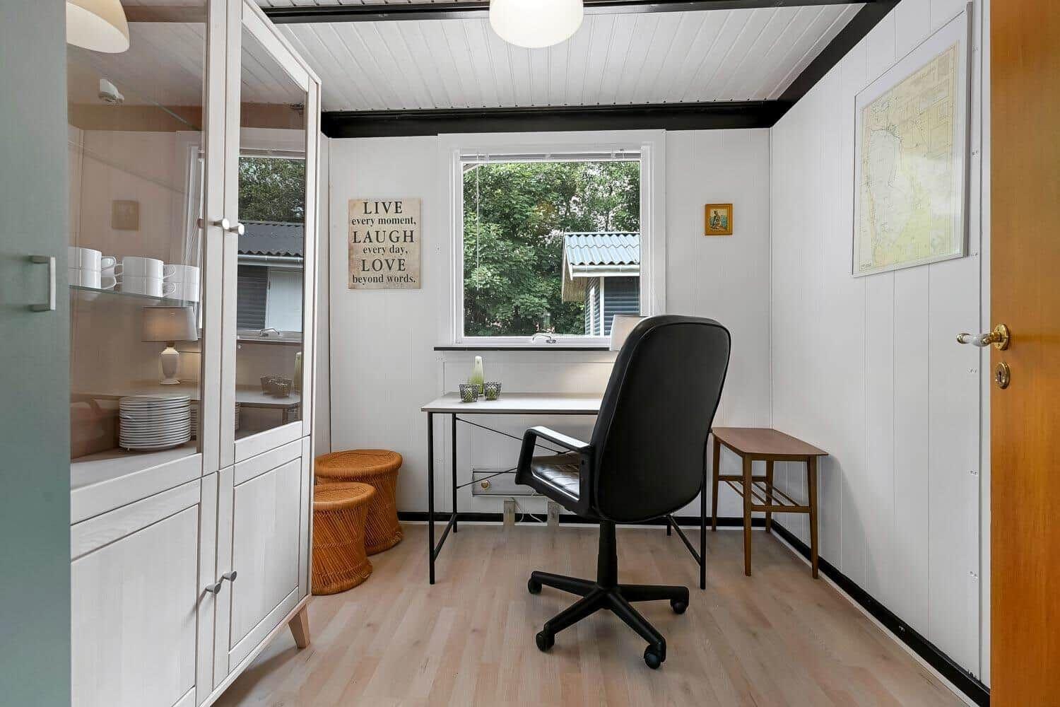 Schreibtisch mit Stuhl und Fenster, daneben Glaswand und Stühle.