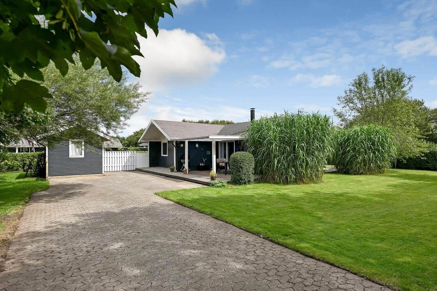 Ein Haus mit Terrasse, Rasen und hohem Gras. Pflasterweg führt zur Eingangstür.
