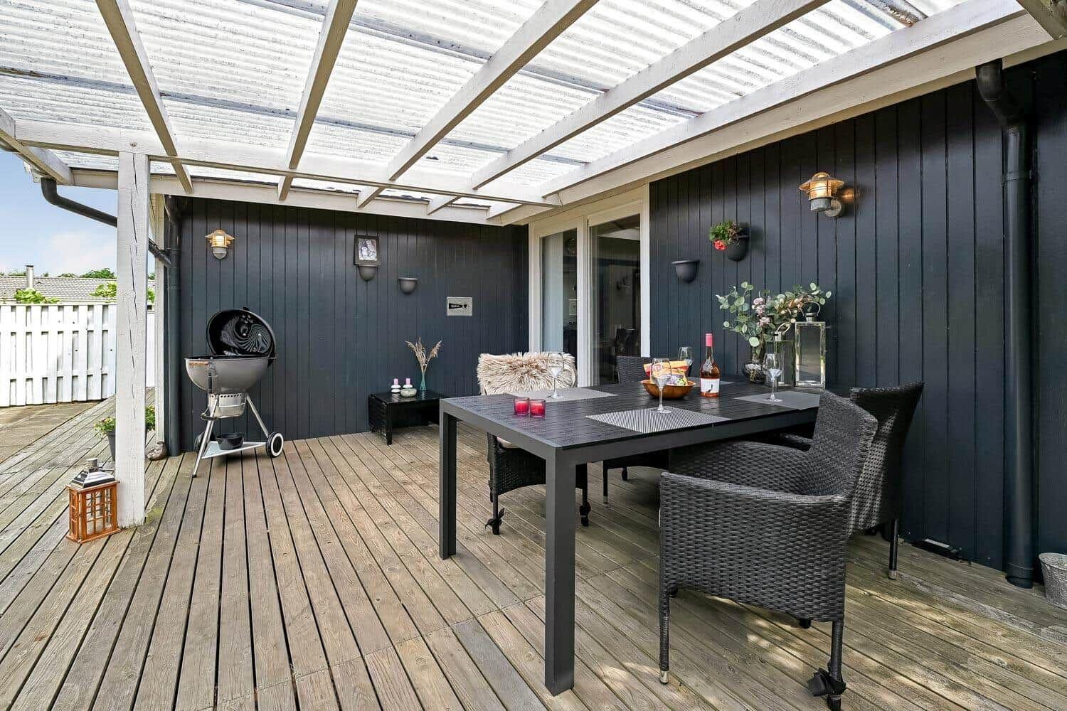 Terrasse mit Grill, Tisch und Stühlen unter Dach.