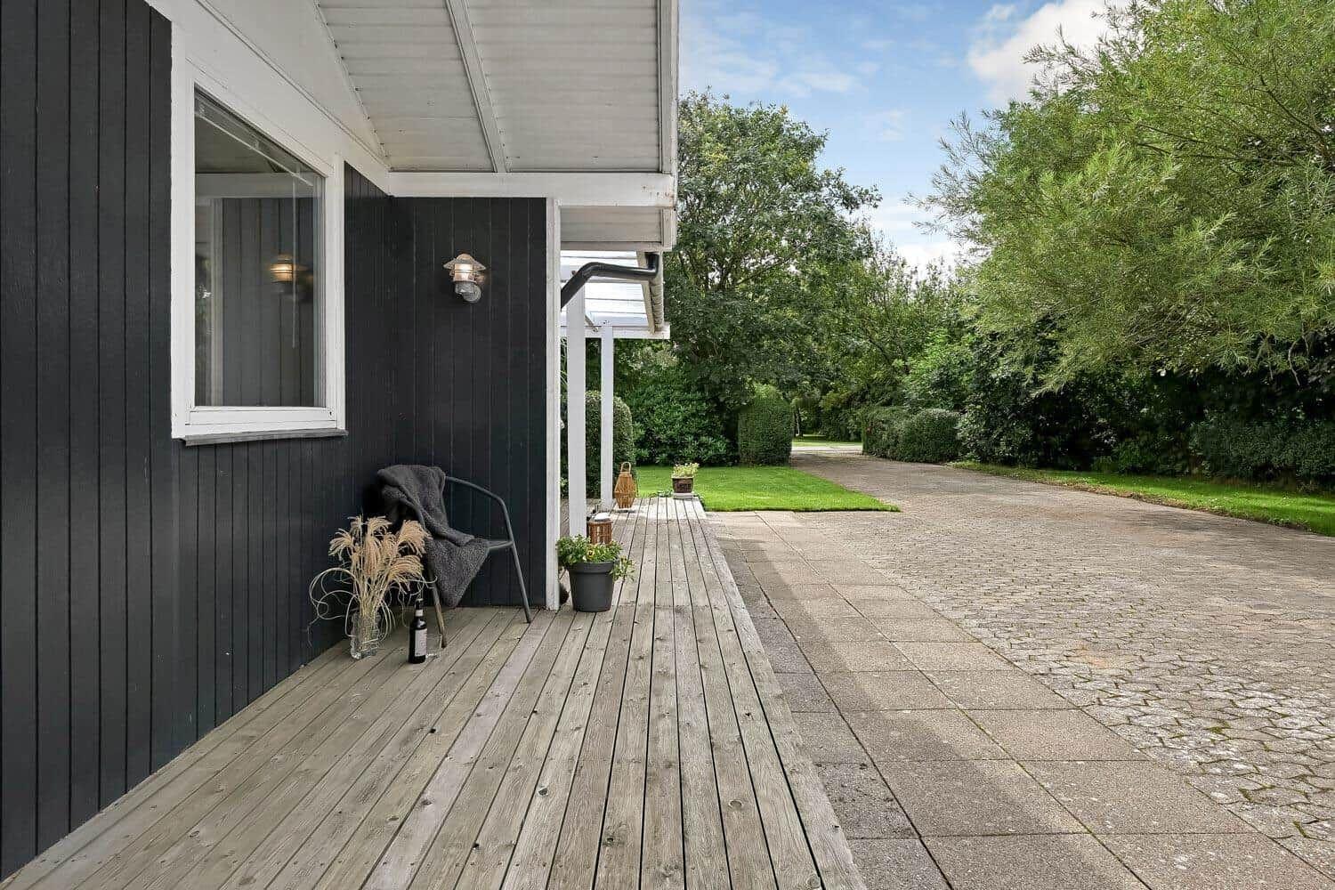 Holzterrasse neben Haus mit Sitzgelegenheit und Blick auf grünen Garten.