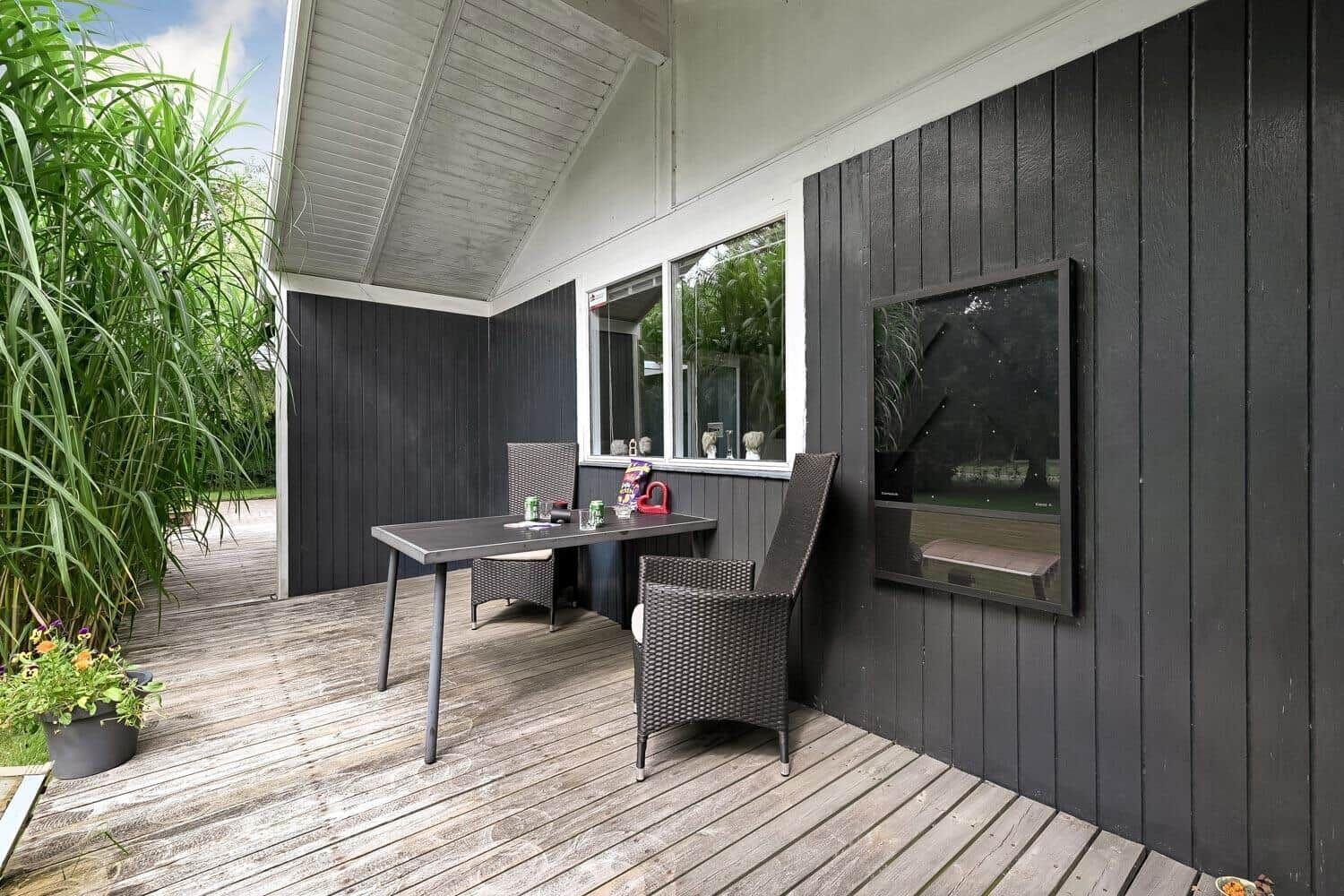 Terrasse mit Tisch und Stühlen, schwarze Holzwände und großes Fenster.