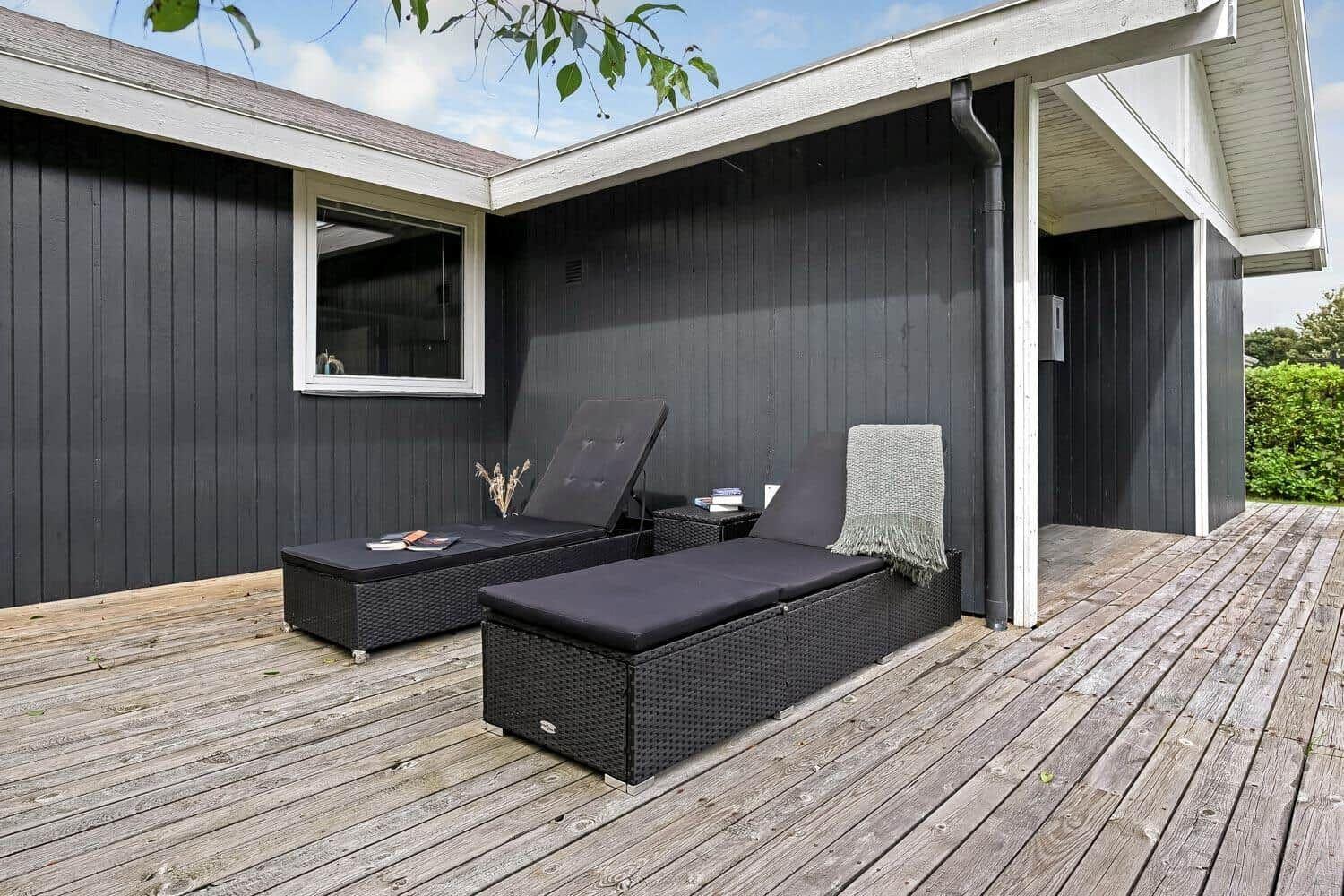 Terrasse mit zwei Liegestühlen und Holzboden vor schwarzem Haus.