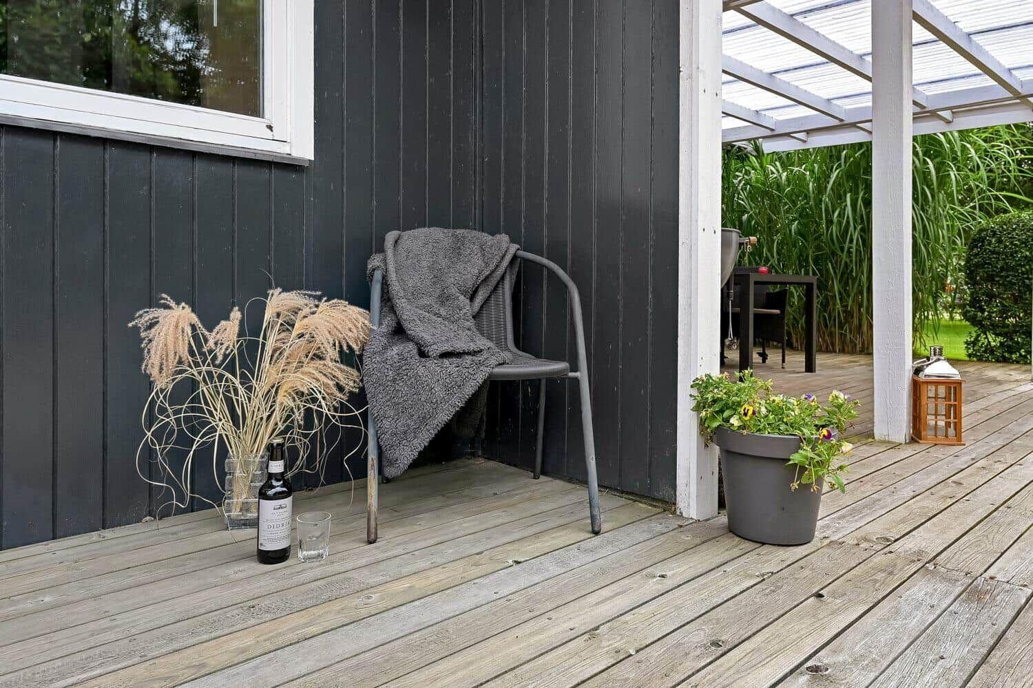 Terrasse mit Stuhl, Decke, Pflanzen und Weinflasche neben Hauswand.