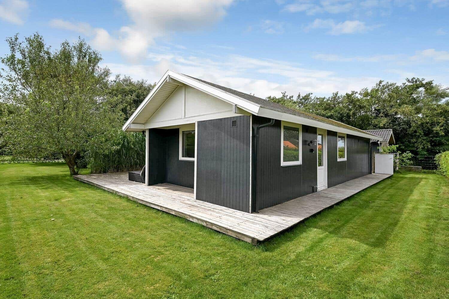 Moderne Hütte mit Holzterrasse und grünem Garten. Fenster und Tür sind weiß.