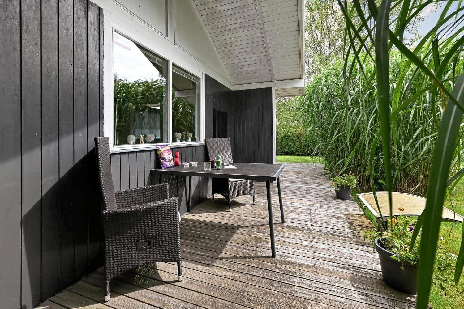 Terrasse mit Tisch, Stühlen und Pflanzen neben Hauswand.