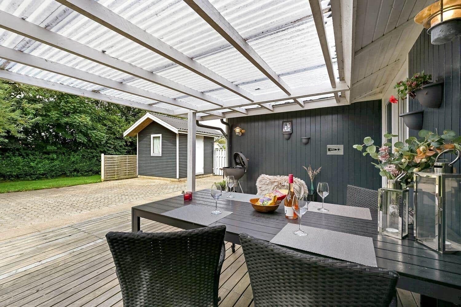 Terrasse mit Tisch, Stühlen und Grill unter Dach