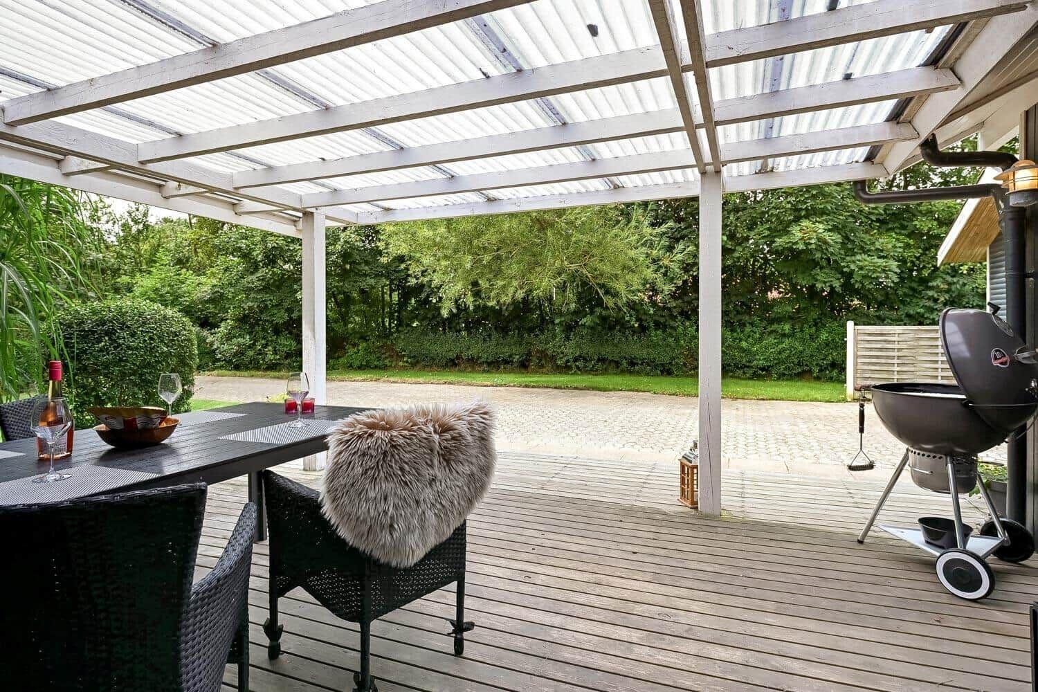 Terrasse mit Tisch, Stühlen und Grill unter Dach.