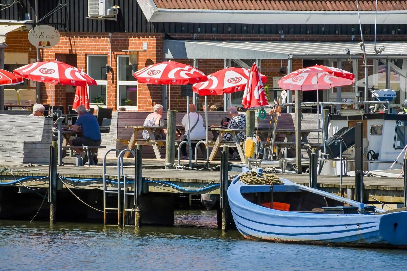 Hafenbecken mit Bootssteg, Tischen und roten Sonnenschirmen.