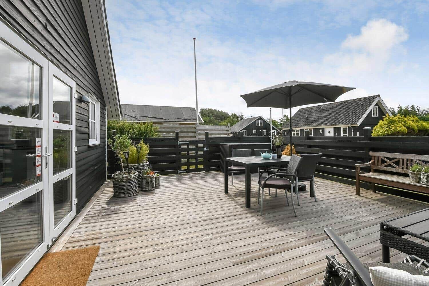 Terrasse mit Tisch, Stühlen und Sonnenschirm. Holzdeck und Gartenmöbel sichtbar.