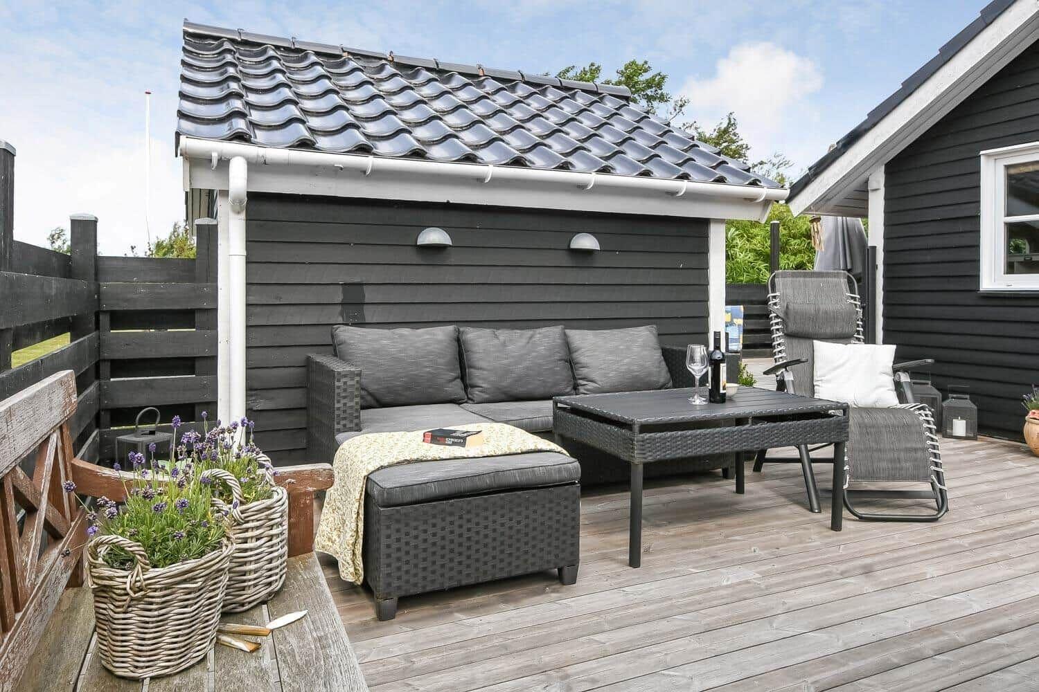 Terrasse mit Sitzgruppe, Tisch und Pflanzen vor schwarzem Holzhaus