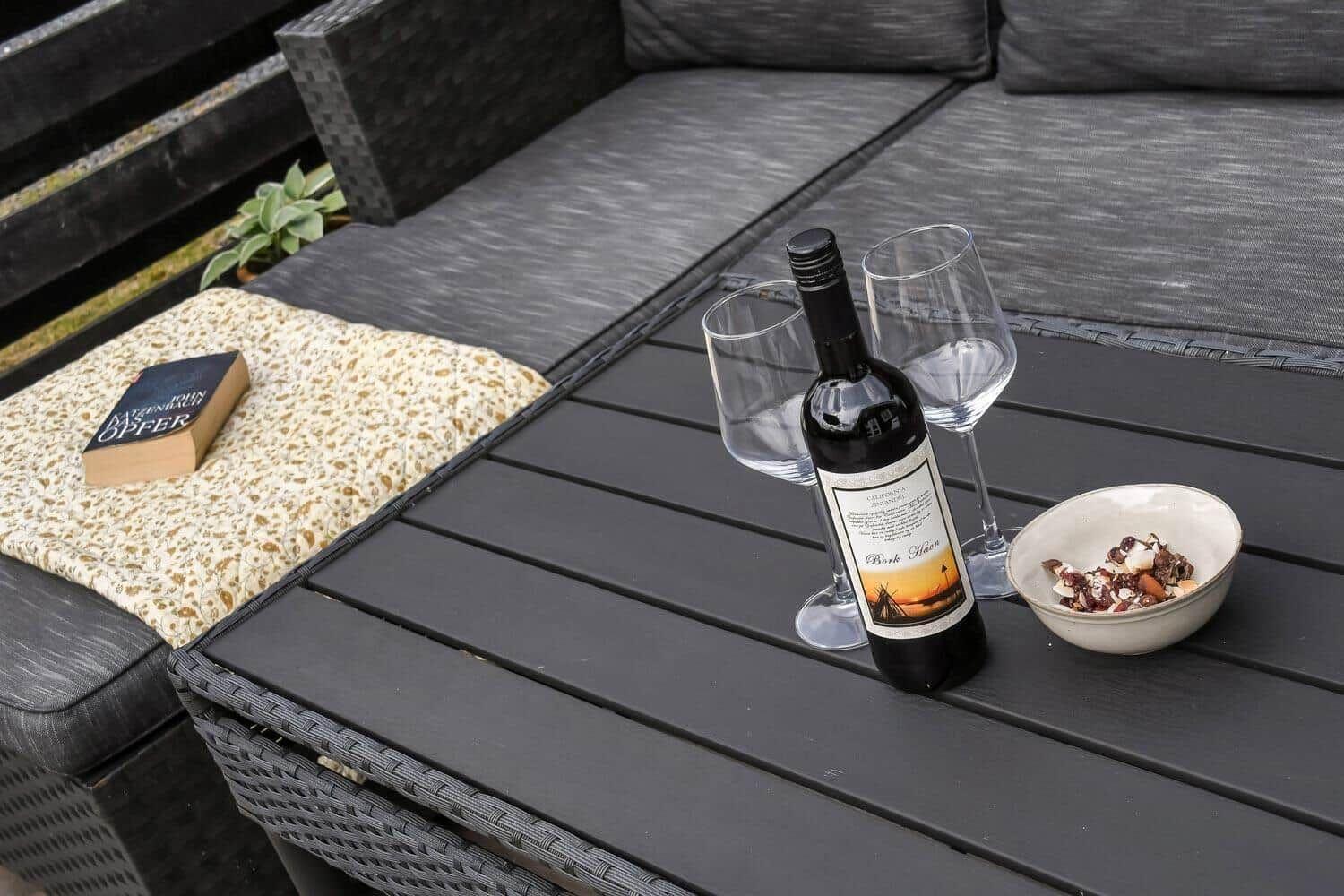 Auf der Terrasse steht ein Tisch mit Wein, Gläsern und einer Schale Nüsse.