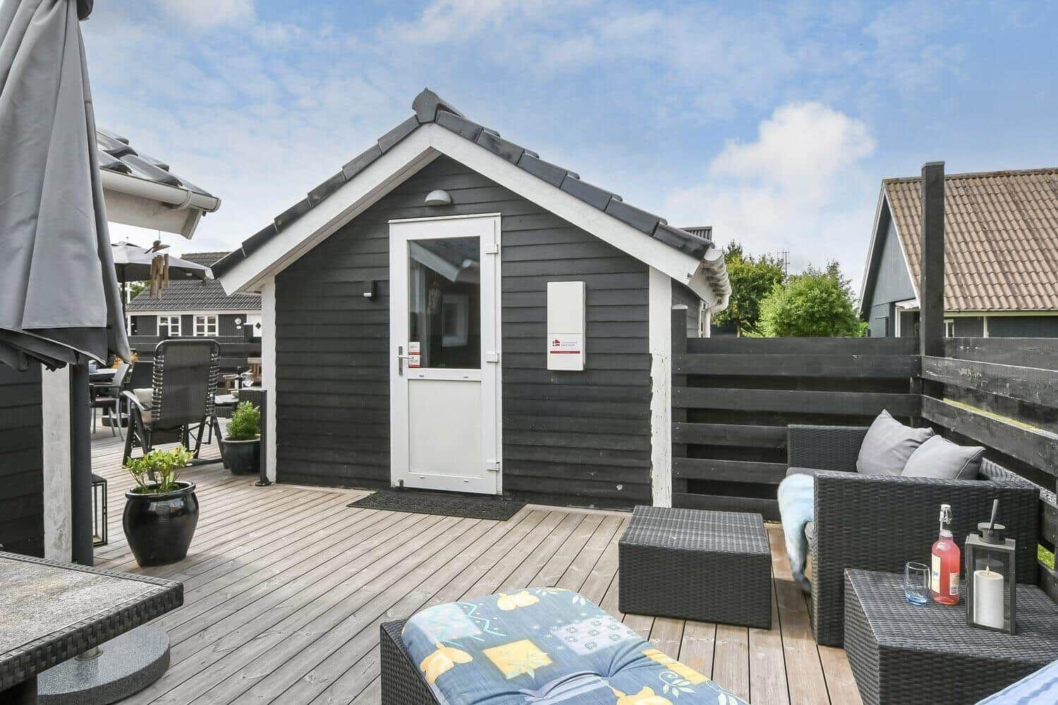 Schwarzes Holzhaus mit weißer Tür und Terrasse mit Gartenmöbeln.