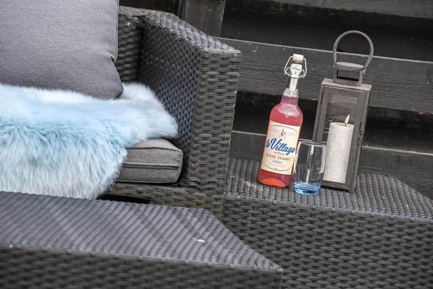 Außenbereich mit Sitzmöbeln, Flasche, Glas und Laterne.