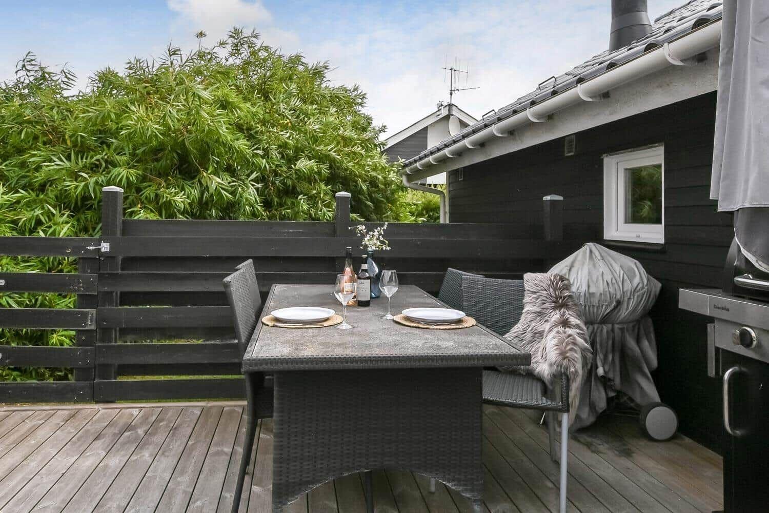 Terrasse mit Tisch, Stühlen, Grill und Blick auf grüne Hecke.