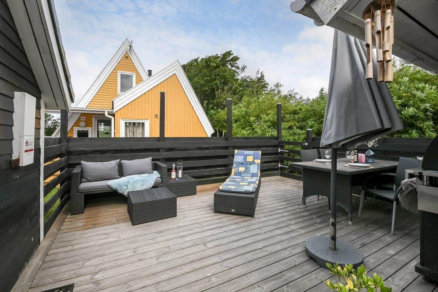 Terrasse mit Sitzgelegenheiten, Tisch und Grill. Im Hintergrund gelbes Haus.