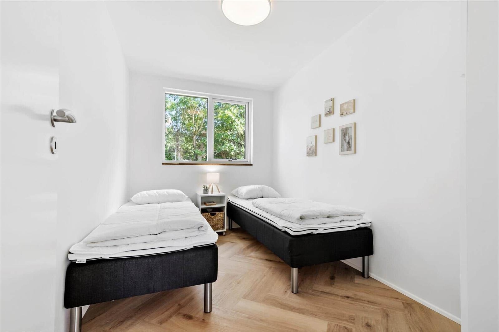 Zwei Einzelbetten, Fenster mit Blick auf Bäume, Wandbilder und Holzboden.