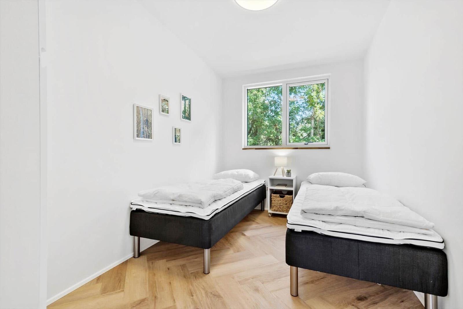 Zwei Betten mit weißer Bettwäsche, Holzboden und Fenster mit Blick auf Bäume.